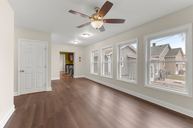 unfurnished living room with dark wood-style flooring, ceiling fan, and baseboards