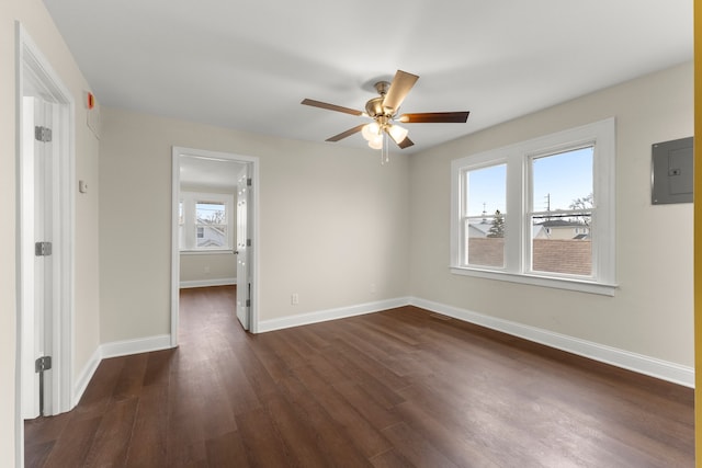 unfurnished room featuring dark wood-type flooring, a ceiling fan, baseboards, and electric panel