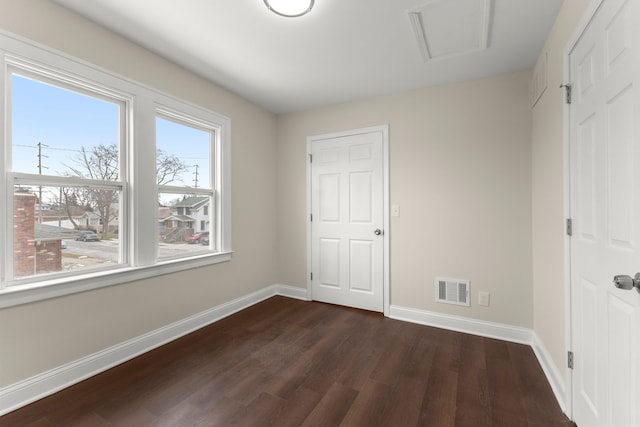 unfurnished bedroom featuring visible vents, attic access, dark wood finished floors, and baseboards
