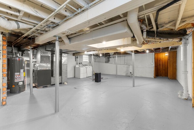 basement featuring washing machine and clothes dryer, heating unit, and water heater