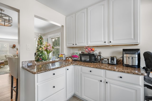 kitchen featuring light hardwood / wood-style floors, white cabinetry, a breakfast bar area, and dark stone countertops