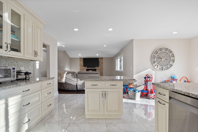 kitchen with cream cabinets, a stone fireplace, light stone counters, and tasteful backsplash