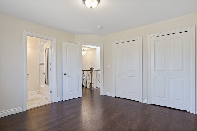 unfurnished bedroom with two closets, connected bathroom, and dark hardwood / wood-style floors