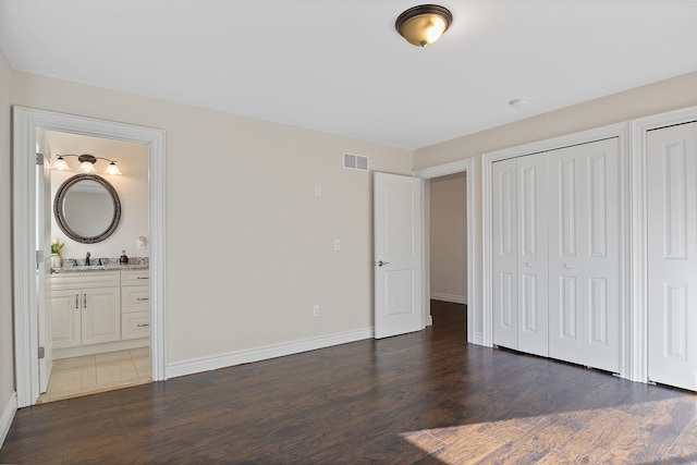 unfurnished bedroom with ensuite bath, two closets, dark hardwood / wood-style flooring, and sink