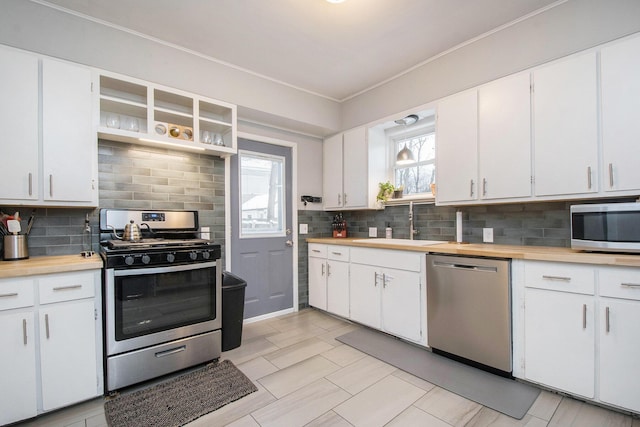 kitchen featuring a wealth of natural light, tasteful backsplash, white cabinets, appliances with stainless steel finishes, and sink