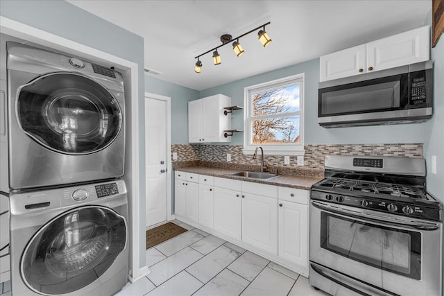 kitchen with appliances with stainless steel finishes, stacked washer / dryer, sink, white cabinets, and decorative backsplash