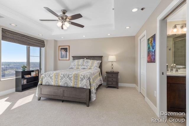 carpeted bedroom featuring sink, ensuite bathroom, ceiling fan, and a tray ceiling