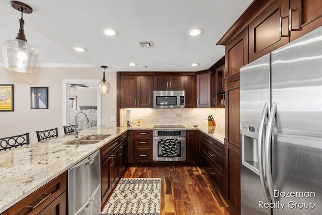 kitchen with appliances with stainless steel finishes, dark wood-type flooring, light stone counters, sink, and decorative light fixtures