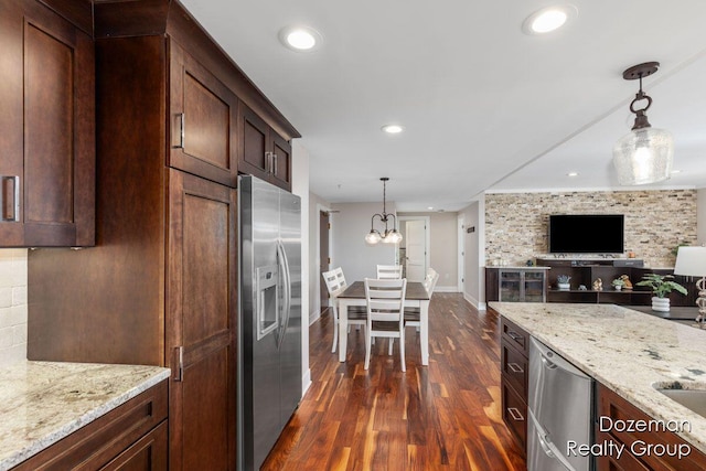 kitchen featuring appliances with stainless steel finishes, decorative light fixtures, an inviting chandelier, light stone counters, and dark wood-type flooring