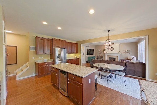 kitchen with stainless steel refrigerator with ice dispenser, a center island, light wood-type flooring, pendant lighting, and light stone countertops