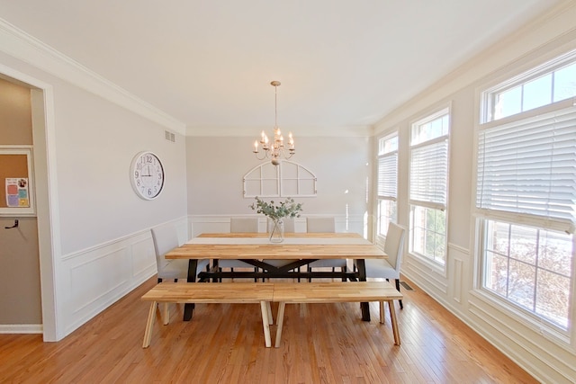 dining area with an inviting chandelier, ornamental molding, and light wood-type flooring