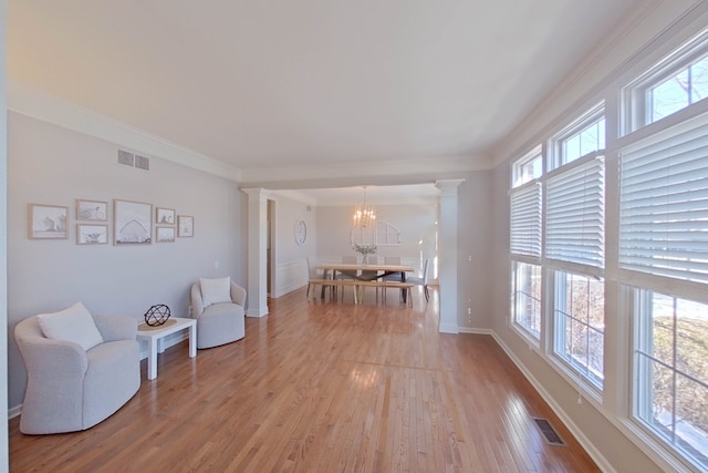 living area with crown molding, a chandelier, light hardwood / wood-style floors, and ornate columns