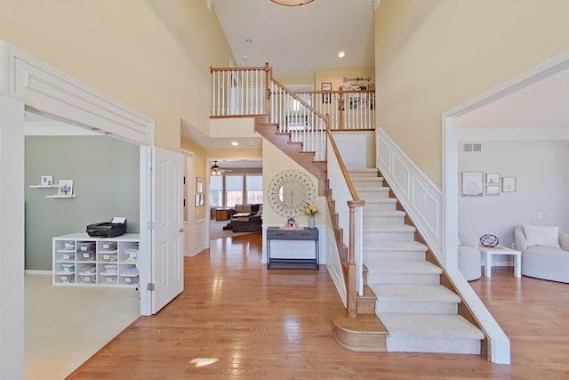 staircase featuring ceiling fan, ornamental molding, hardwood / wood-style floors, and a high ceiling