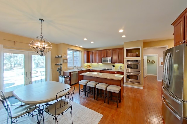 kitchen featuring pendant lighting, light hardwood / wood-style flooring, stainless steel appliances, light stone countertops, and a kitchen island