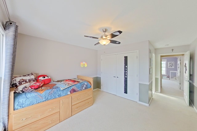 bedroom featuring light colored carpet, ceiling fan, and a closet