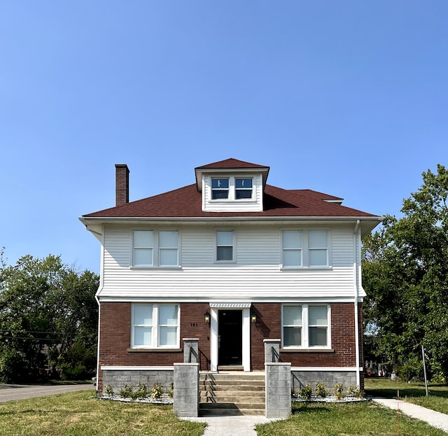 american foursquare style home featuring brick siding, a front yard, and a chimney