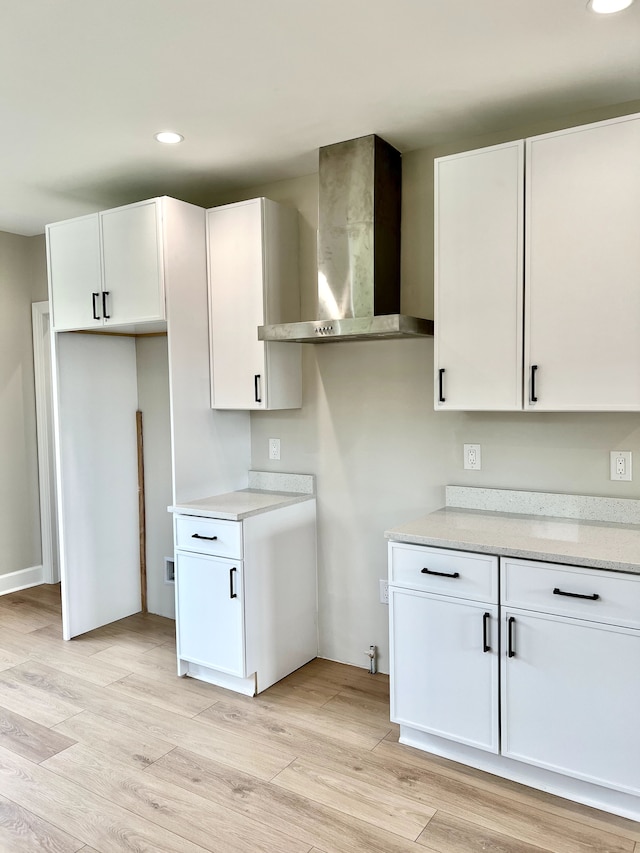 kitchen with white cabinets, wall chimney range hood, and light hardwood / wood-style floors