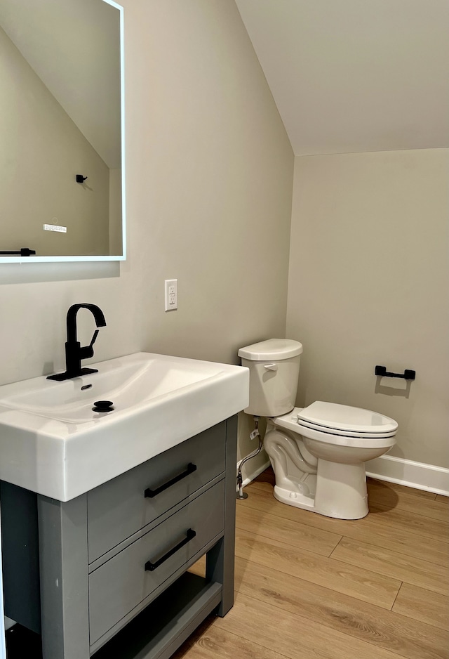 bathroom with hardwood / wood-style floors, lofted ceiling, vanity, and toilet