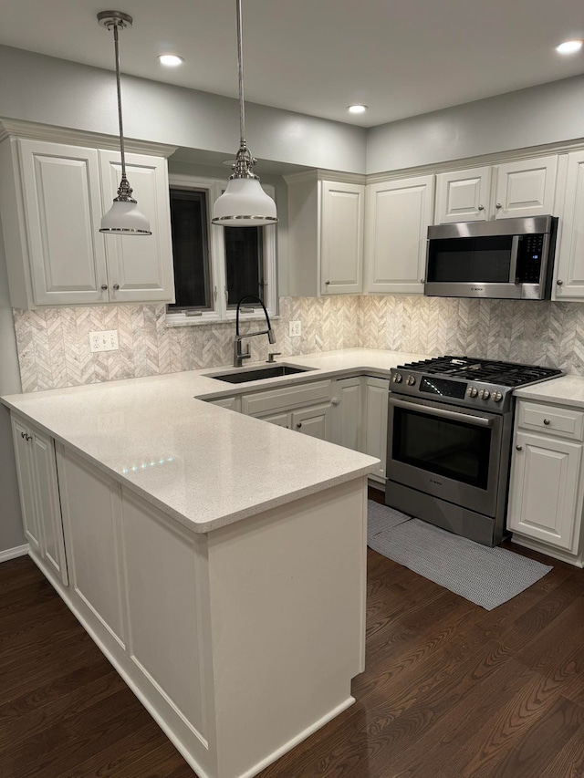 kitchen with kitchen peninsula, appliances with stainless steel finishes, hanging light fixtures, white cabinets, and sink