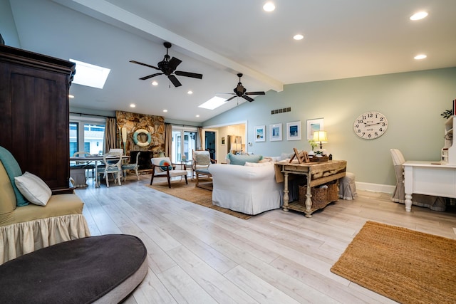 living room with light wood-type flooring, ceiling fan, vaulted ceiling with skylight, and a stone fireplace