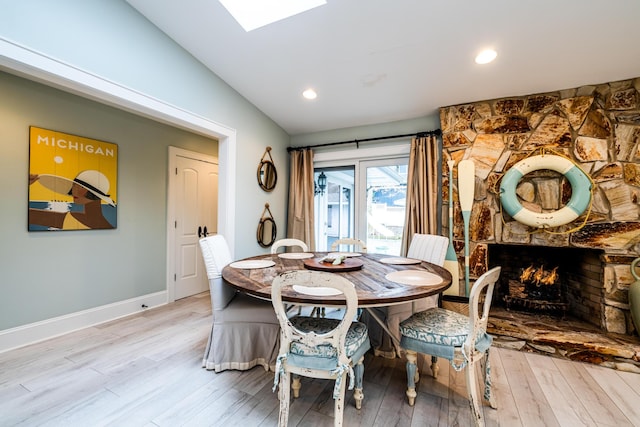 dining space featuring light wood-type flooring, vaulted ceiling with skylight, and a stone fireplace