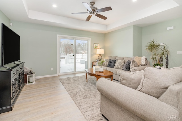 living room featuring ceiling fan, a tray ceiling, and light hardwood / wood-style flooring