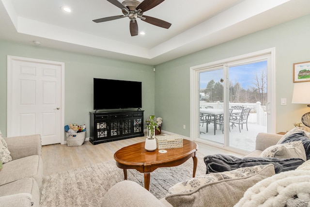 living room with ceiling fan, a tray ceiling, and light hardwood / wood-style floors