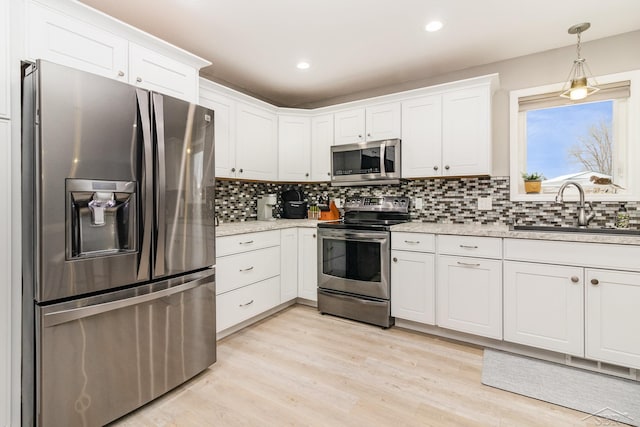 kitchen with stainless steel appliances, white cabinetry, sink, and light stone counters