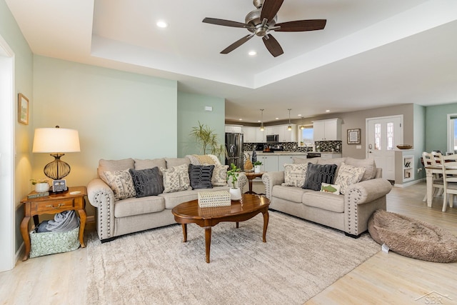 living room featuring a raised ceiling, ceiling fan, and light wood-type flooring