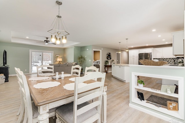 dining space with ceiling fan with notable chandelier, a tray ceiling, light hardwood / wood-style floors, and sink