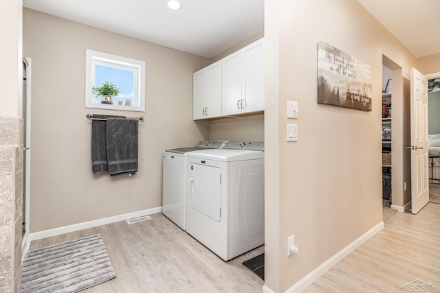 clothes washing area with light hardwood / wood-style flooring, cabinets, and washer and clothes dryer