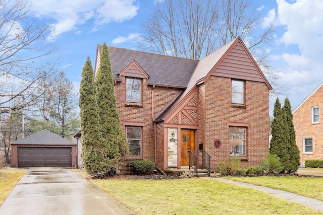 english style home with brick siding, a detached garage, a front lawn, and an outdoor structure