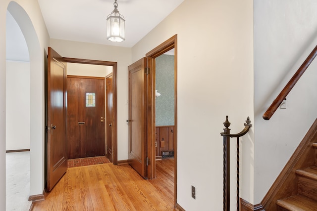 hallway featuring arched walkways, wood walls, stairway, and light wood finished floors