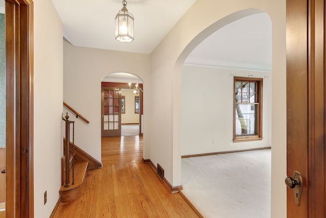 hall featuring light wood finished floors, baseboards, visible vents, and arched walkways