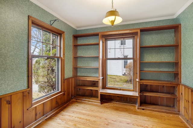 unfurnished dining area featuring wallpapered walls, light wood finished floors, wainscoting, and crown molding