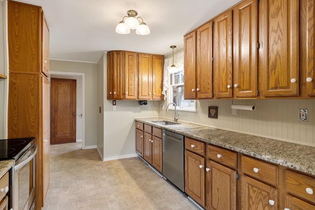 kitchen with appliances with stainless steel finishes, brown cabinetry, a sink, light stone countertops, and baseboards