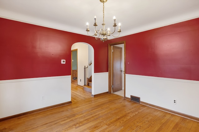 unfurnished room featuring a wainscoted wall, visible vents, arched walkways, and wood finished floors