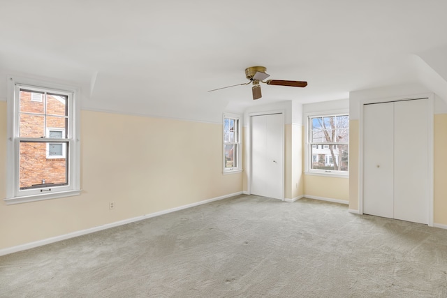 unfurnished bedroom with carpet floors, a ceiling fan, baseboards, and multiple closets