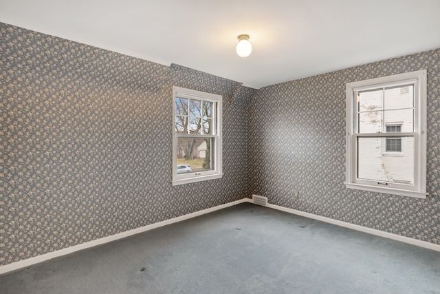 carpeted empty room featuring baseboards, wallpapered walls, visible vents, and a healthy amount of sunlight