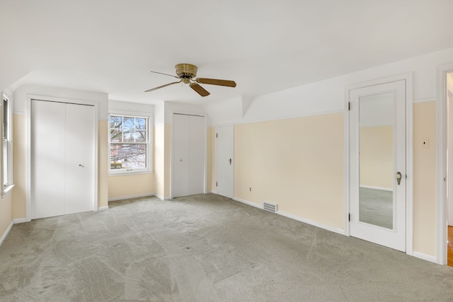 unfurnished bedroom featuring ceiling fan, carpet floors, visible vents, baseboards, and multiple closets