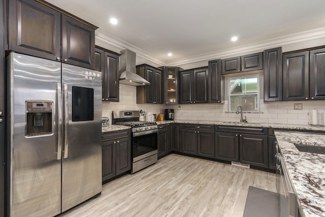 kitchen featuring stainless steel appliances, light wood-type flooring, light stone counters, wall chimney exhaust hood, and backsplash