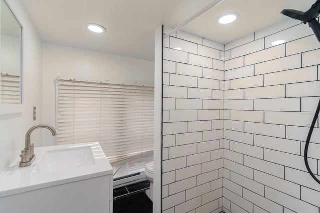 bathroom with a tile shower, vanity, toilet, and a baseboard heating unit