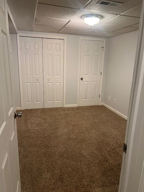 unfurnished bedroom with a closet, carpet flooring, and a drop ceiling