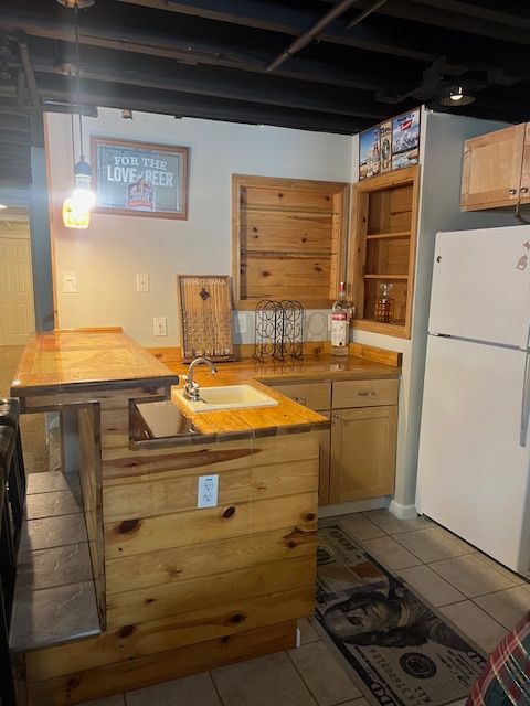 kitchen featuring sink, white refrigerator, wooden counters, and light tile patterned floors