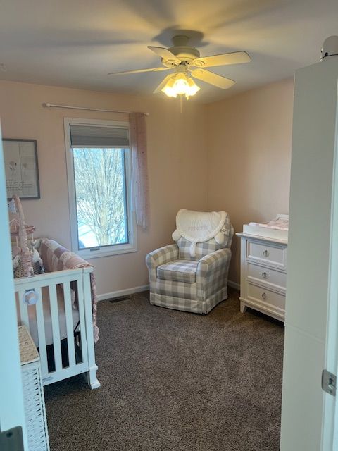 carpeted bedroom featuring a nursery area and ceiling fan