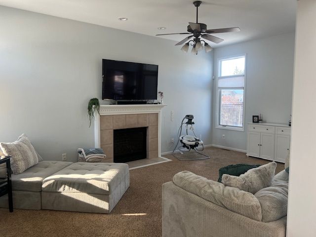 carpeted living room with a tiled fireplace and ceiling fan