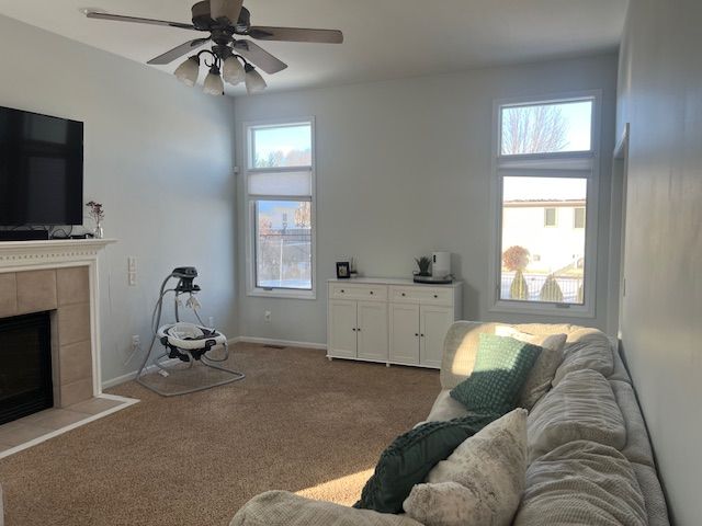 living room featuring a tile fireplace, carpet floors, and ceiling fan