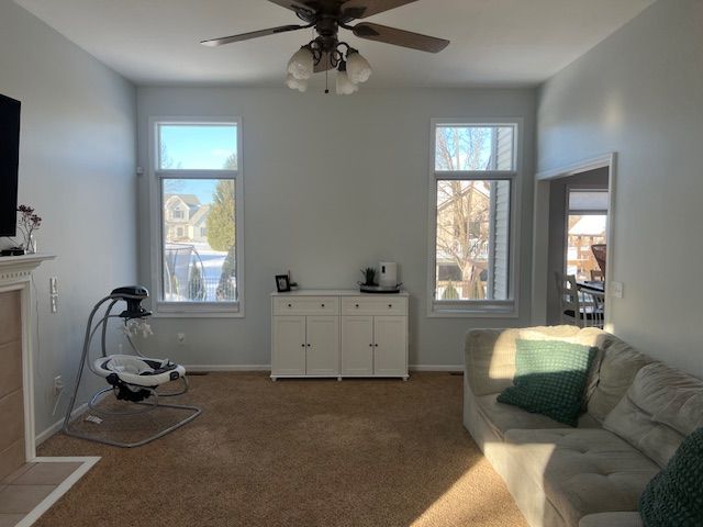 living room featuring ceiling fan, a tiled fireplace, and carpet floors