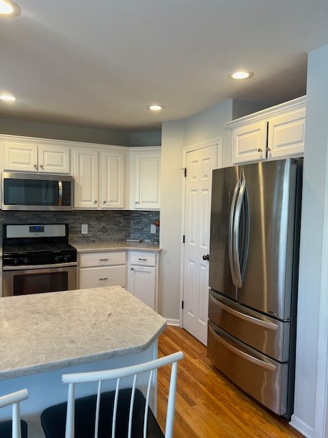 kitchen with appliances with stainless steel finishes, white cabinets, decorative backsplash, and wood-type flooring