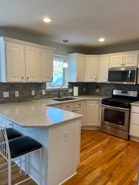 kitchen with appliances with stainless steel finishes, kitchen peninsula, pendant lighting, sink, and white cabinetry